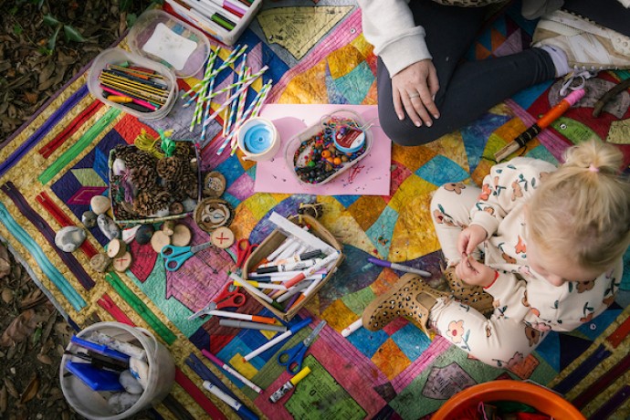 A toddler playing with art supplies on a colourful mat in the forest.